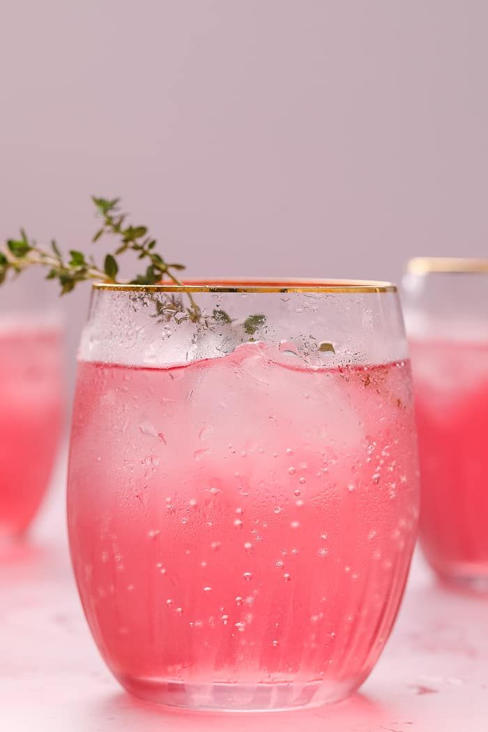 two glasses filled with pink liquid and garnished with small green sprigs