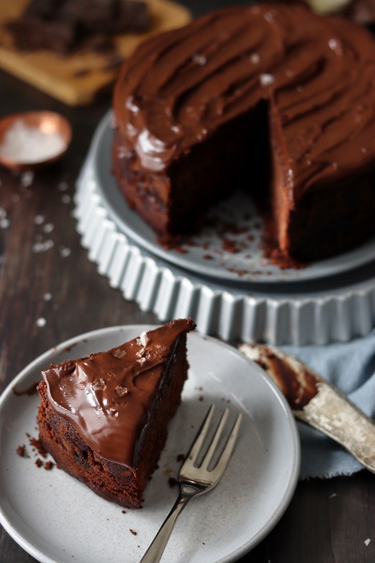 a piece of chocolate cake on a white plate with a knife and fork next to it