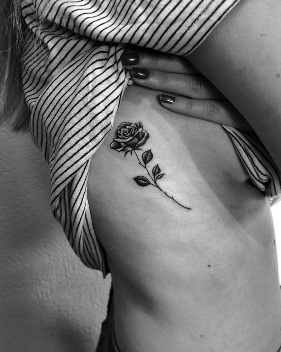 a woman's stomach with a rose tattoo on her left side ribcage