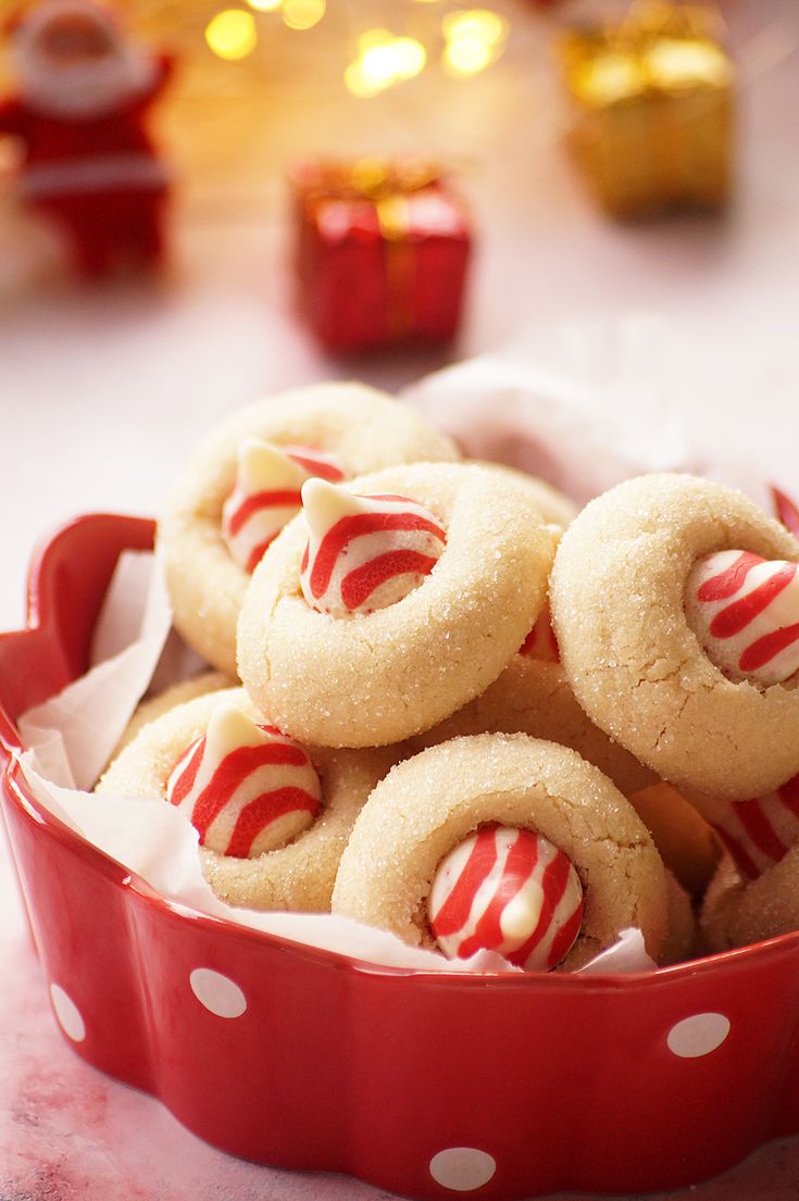 a red and white polka dot bowl filled with cookies on top of a table next to christmas lights