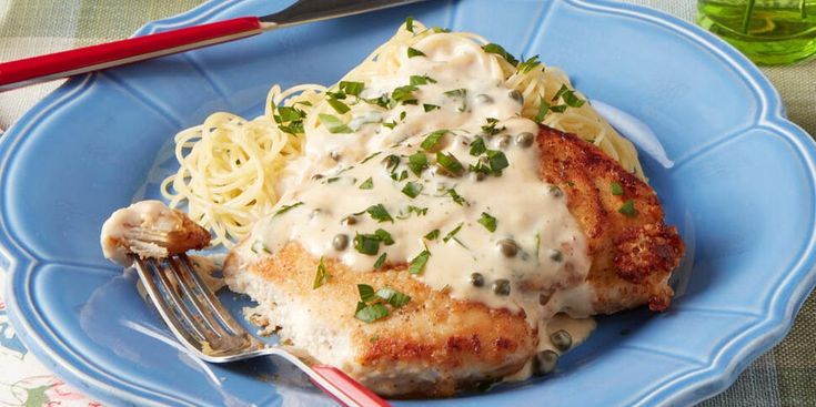 a blue plate topped with meat covered in gravy next to pasta and a fork