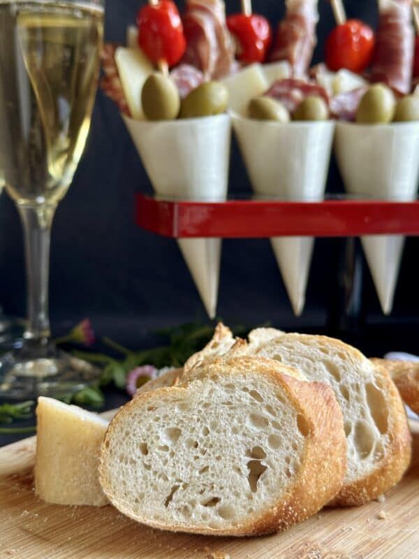 bread and cheese on a cutting board with glasses of wine in the backround