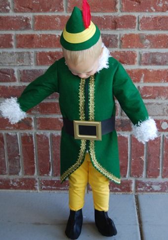 a doll dressed in green and yellow stands next to a brick wall with his hands on his hips