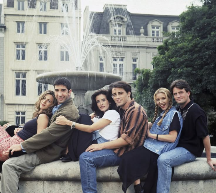 a group of young people sitting on top of a fountain in front of a building