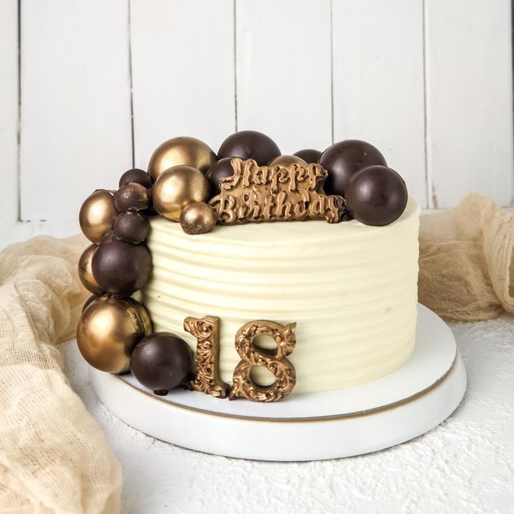 a birthday cake decorated with chocolate and gold decorations on a white plate next to a wooden wall