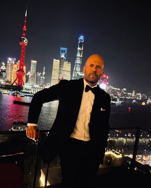 a man in a tuxedo stands on a balcony overlooking the city at night