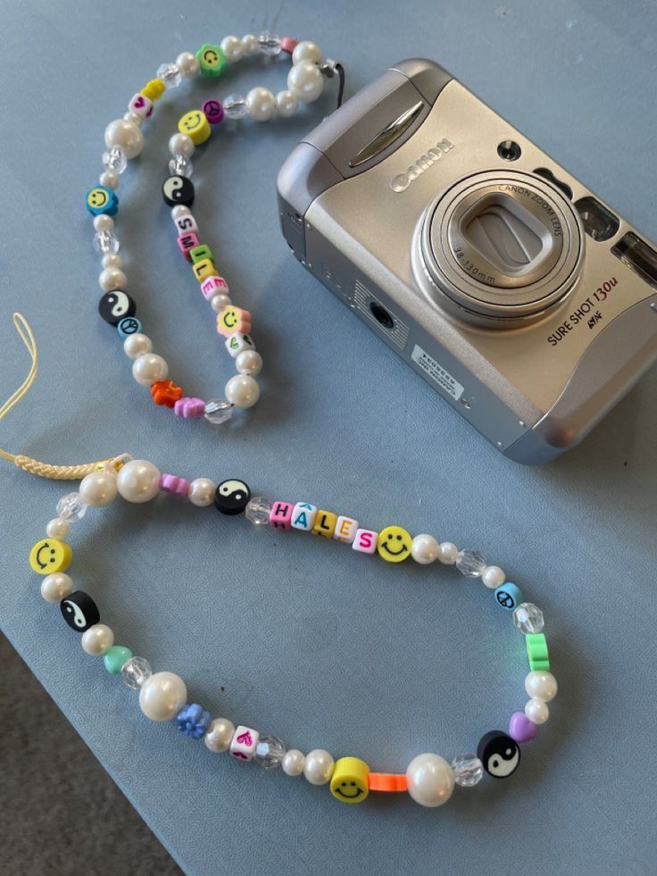 a camera and some beads are laying on the table next to a necklace with smiley faces