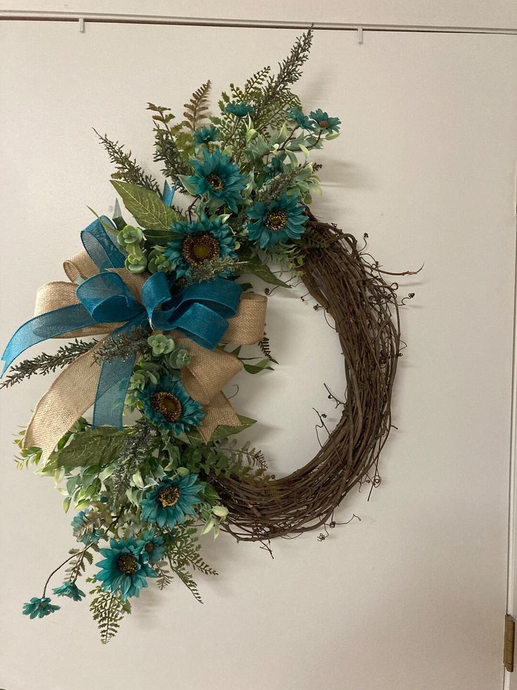 a wreath with blue flowers and greenery hanging on the wall next to a door