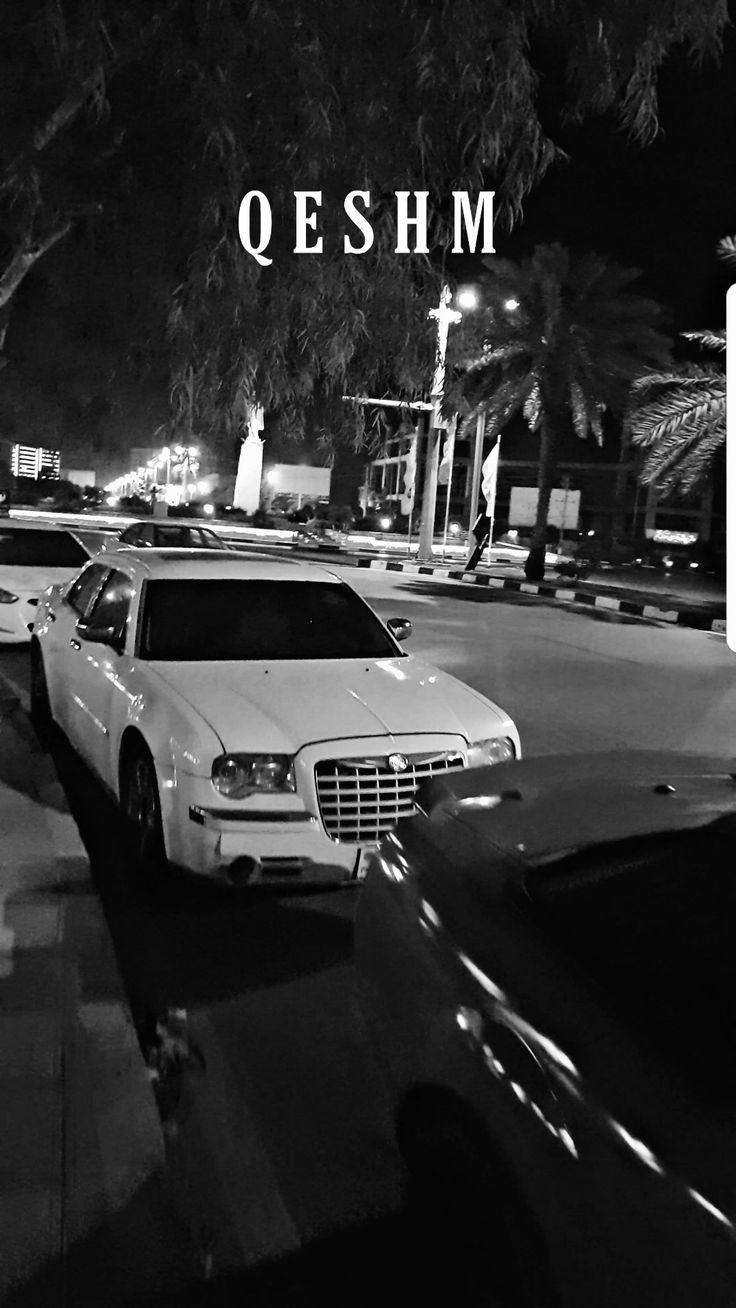 black and white photograph of cars parked on the side of a road at night time