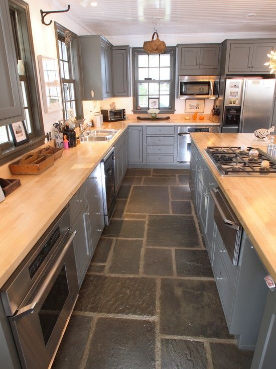 a kitchen with gray cabinets and stone flooring