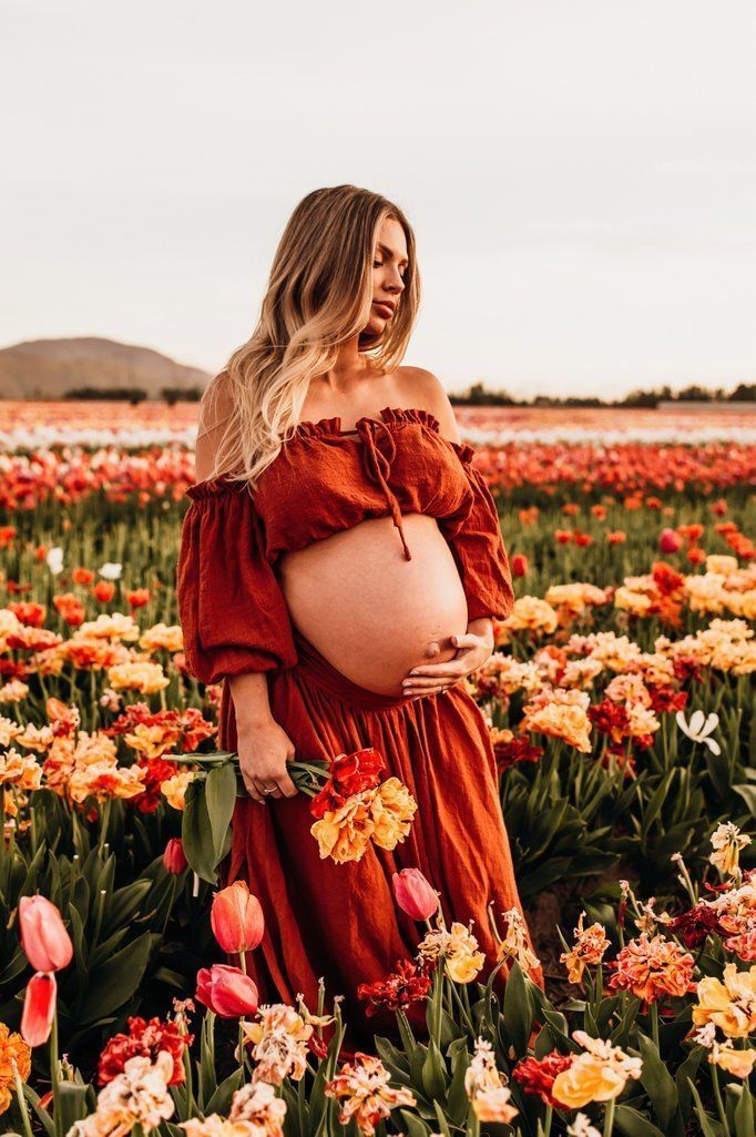 a pregnant woman standing in a field of flowers wearing an off the shoulder red dress