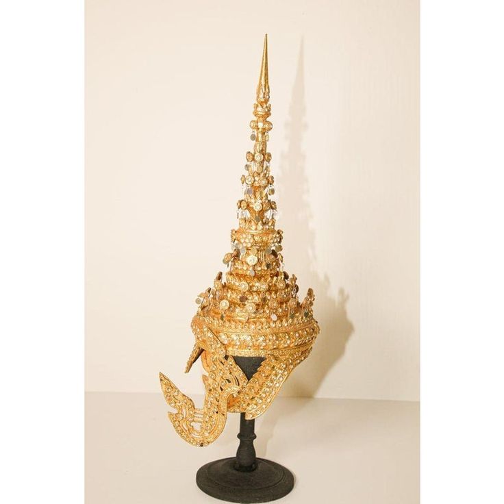 Ceremonial Thai headdress usually worn for wedding or religious ceremonies. Hand-crafted in Thailand. Gilt Thai Ceremonial Headdress circa 20th century. A traditionally modeled design with a conical metal spire at the top, in gilt papier mâché, metal and glass gemstones displayed on a black wooden stand. Dimensions: H 26 in. x W 11 in. x D 9 in. Gold Ceremonial Headpiece With Tall Crown, Traditional Ceremonial Headpieces For Festivals, Traditional Gold Ceremonial Headpieces, Traditional Gold Headpiece With Tall Crown, Traditional Ceremonial Headpiece With Pinched Crown, Ceremonial Tall Crown Headpiece For Festivals, Traditional Gold Crown Headpiece, Traditional Gold Headpiece With Structured Crown, Traditional Gold Structured Crown Headpiece