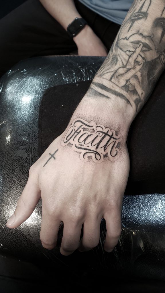 a man with a cross tattoo on his arm and hand is sitting in a chair