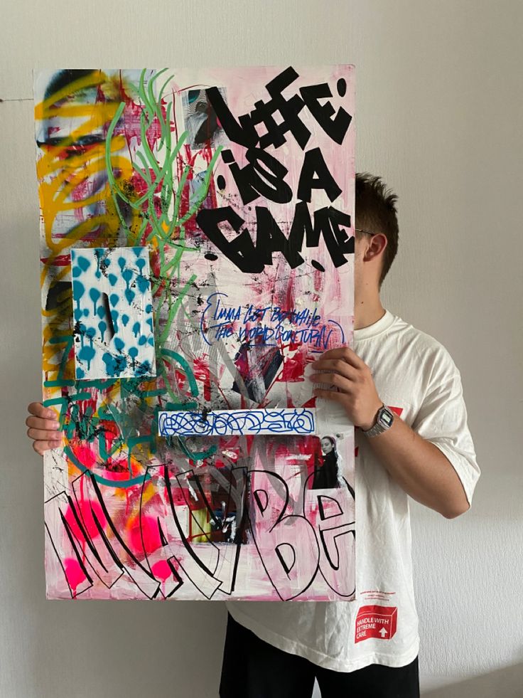 a man holding up a large piece of art with graffiti on it's sides