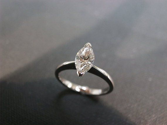 an engagement ring with a pear shaped diamond on it's side, sitting on a black surface