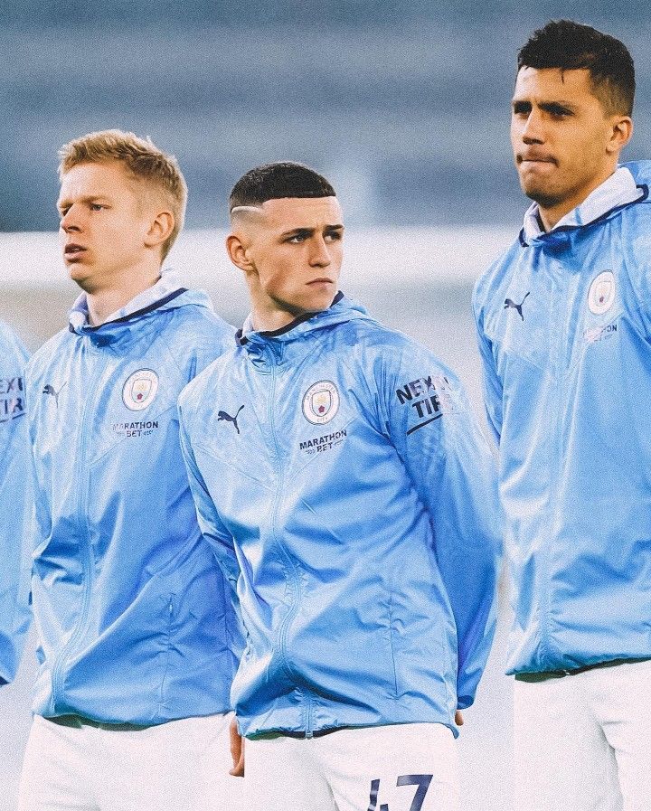 three men in blue jackets standing next to each other on a soccer field with one man looking at the camera