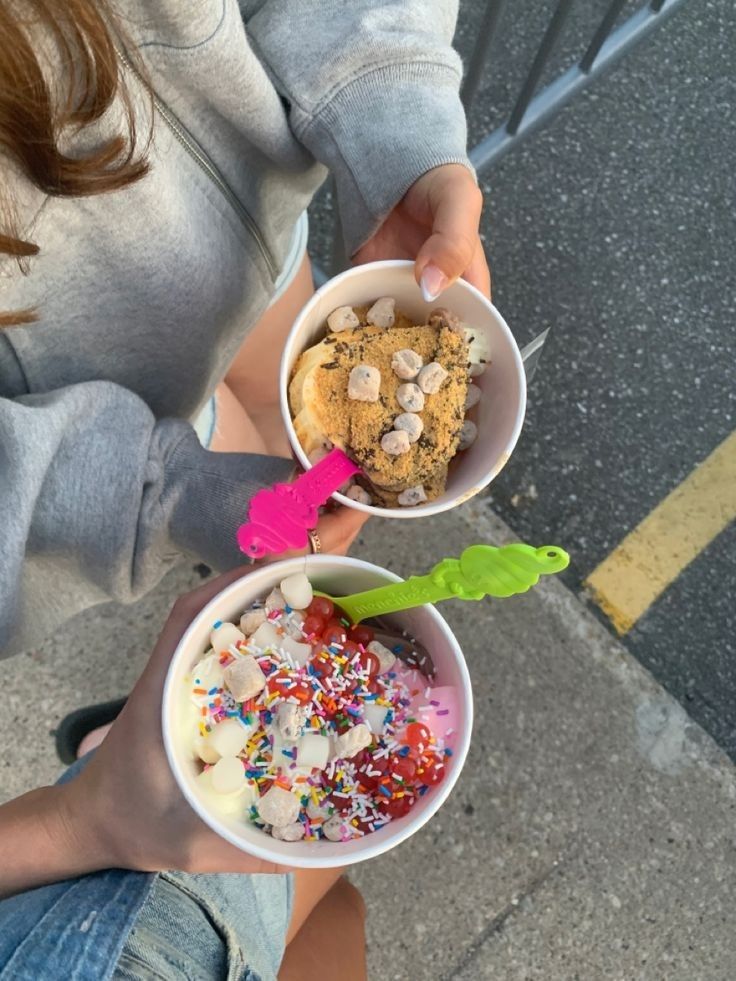 a woman holding two bowls filled with ice cream and sprinkles