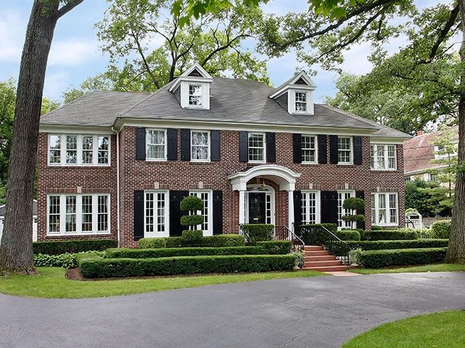 a large brick house with black shutters and white trim on the windows, surrounded by trees