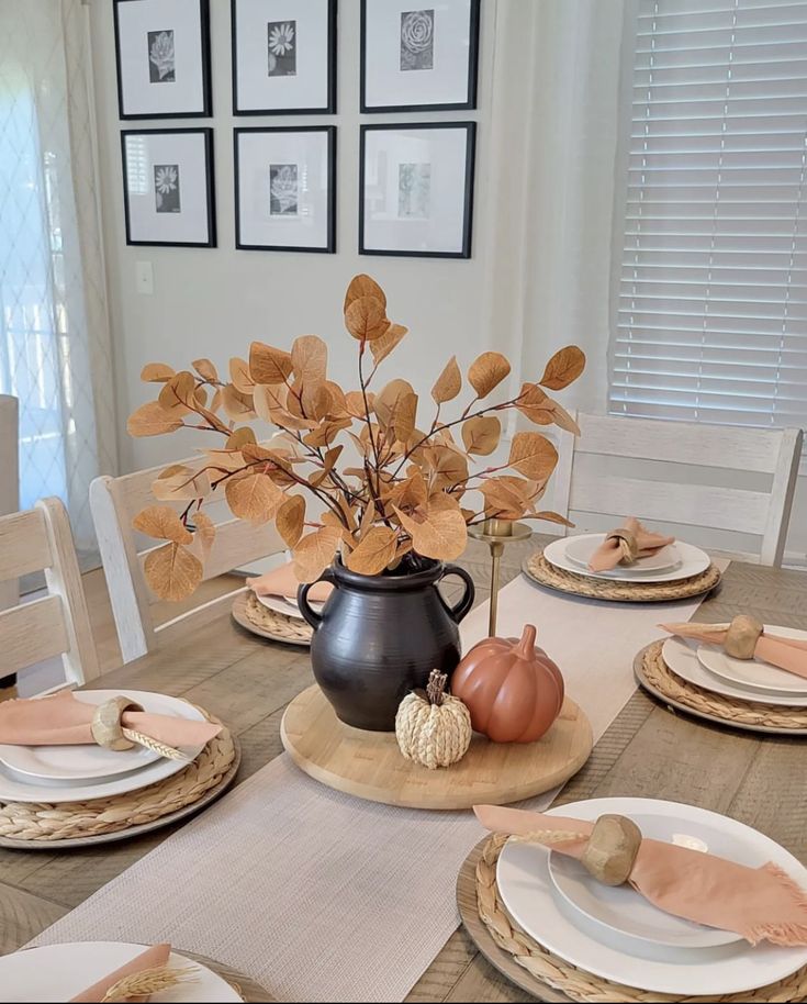 a dining room table set with plates and place settings for thanksgiving dinner, including pumpkins