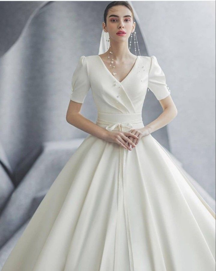 a woman in a white wedding dress with pearls on her neck and sleeves, standing against a