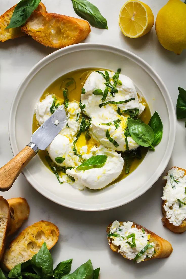 a white bowl filled with food next to lemons and bread on top of a table