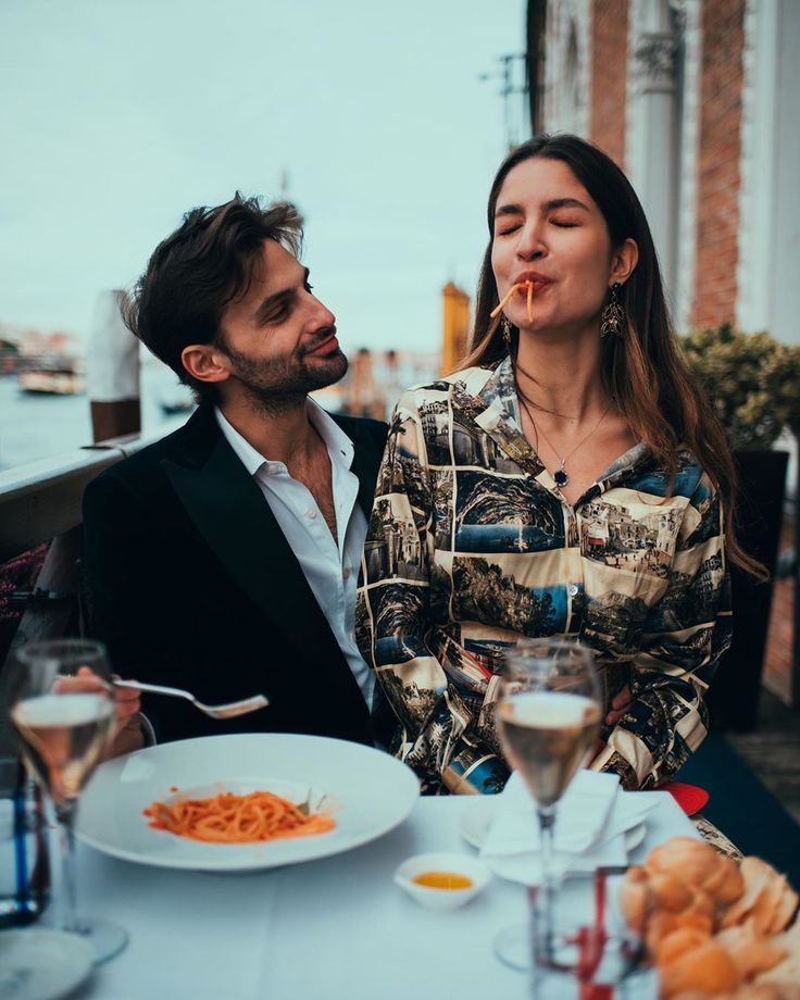 two people sitting at a table with food and drinks in front of them, one is blowing bubbles