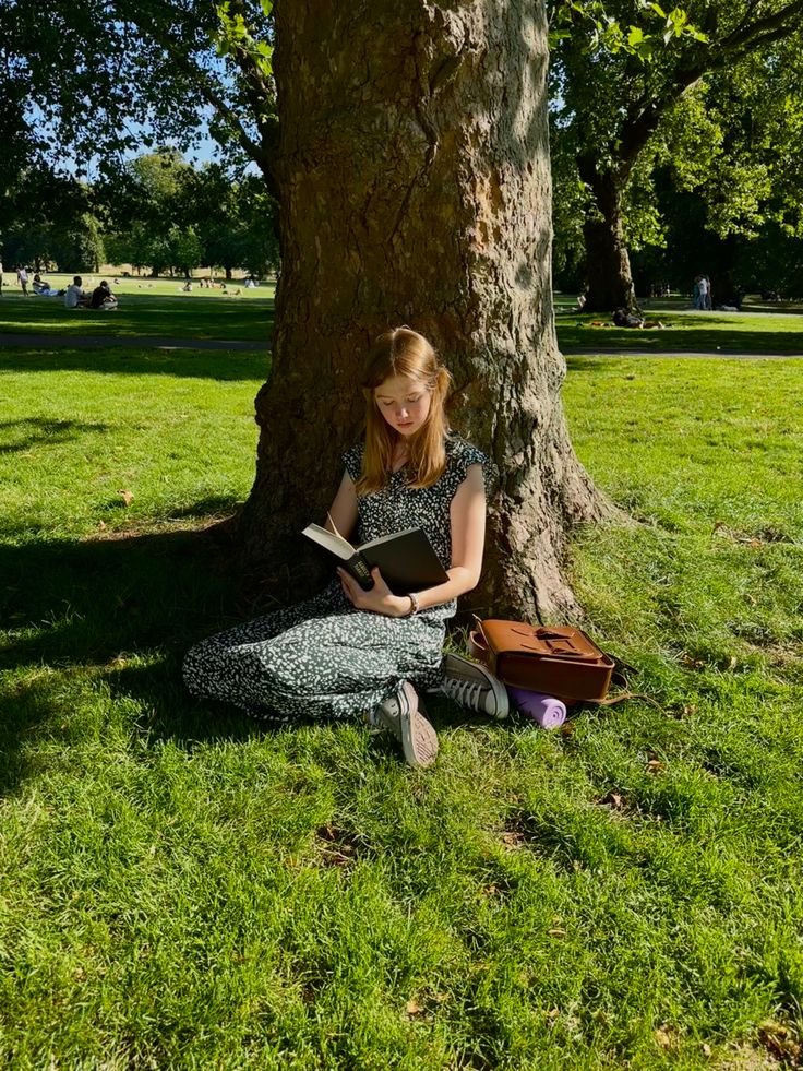 a woman sitting under a tree reading a book