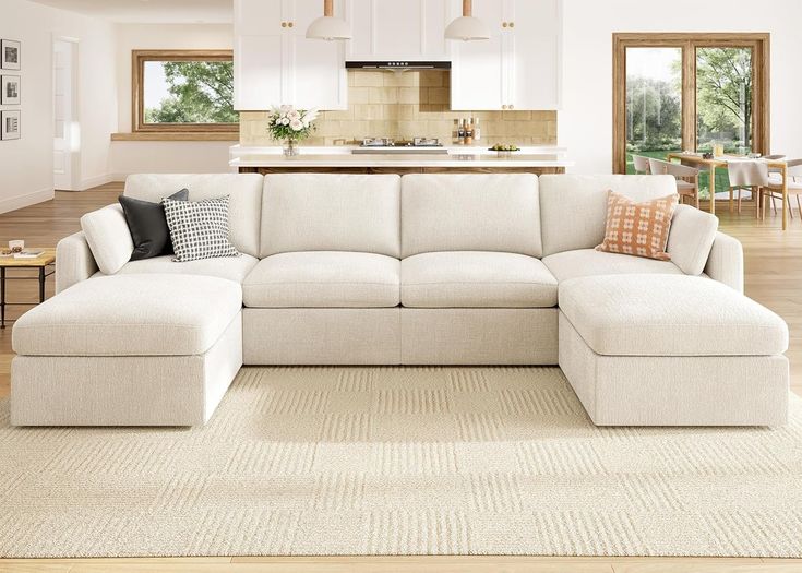 a large white sectional couch in a living room with hardwood flooring and open kitchen