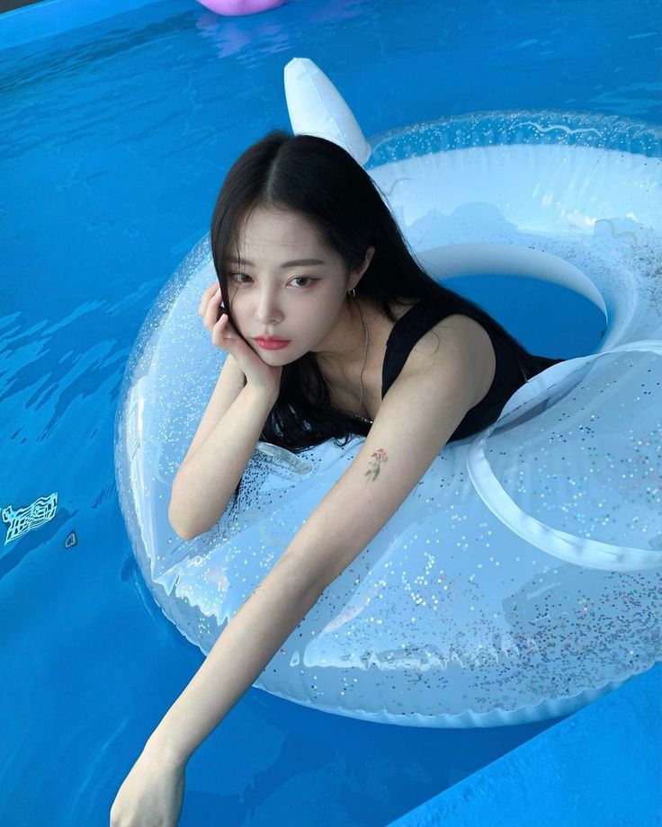 a woman in a black bathing suit floating on an inflatable raft next to a swimming pool