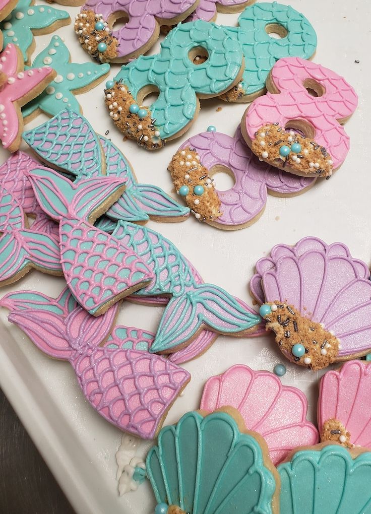 some decorated cookies are sitting on a table with mermaid tail and seashells around them