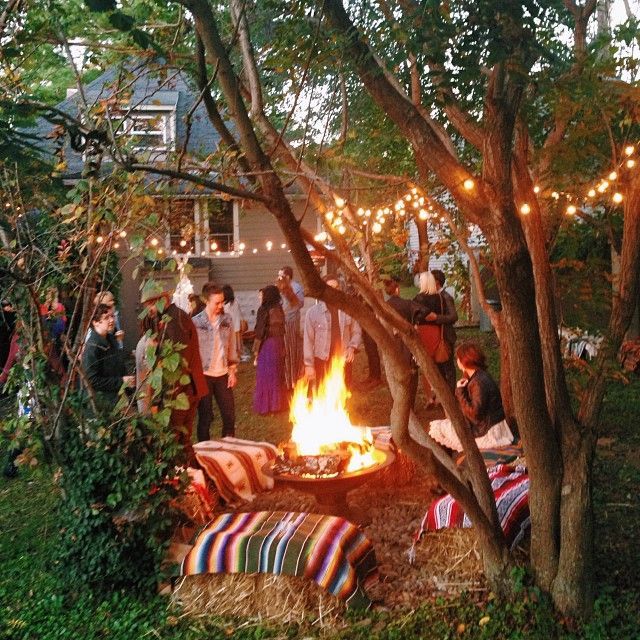 a group of people gathered around a fire pit in the yard with lights strung over it