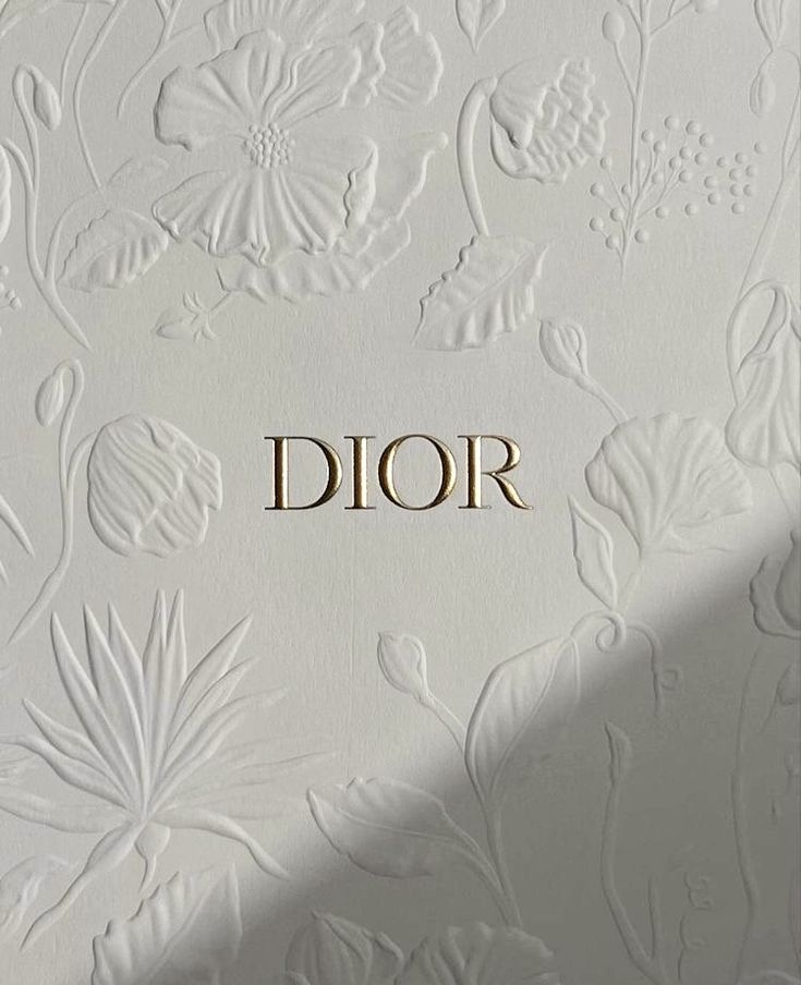 the word dior written in gold letters on a white wall with floral designs and leaves