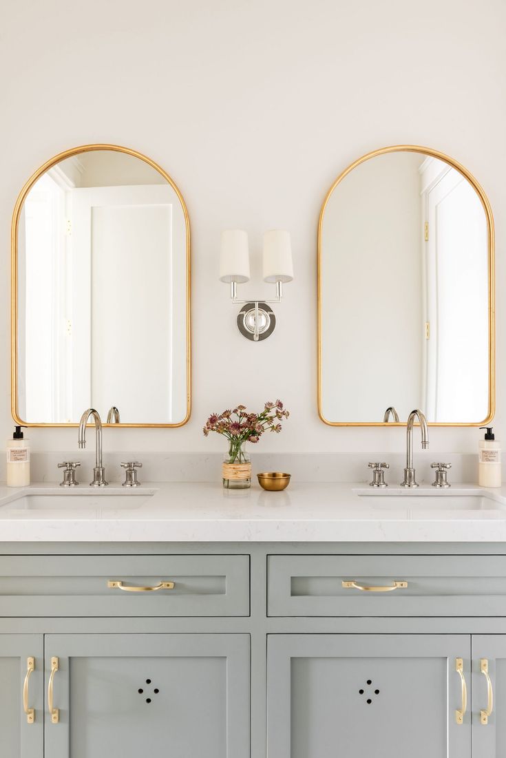 two mirrors are above the double sinks in this white and gold bathroom with brass accents