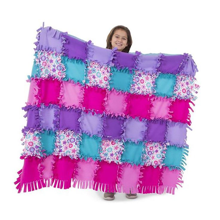 a woman holding up a blanket made out of purple, blue and pink squares with fringes