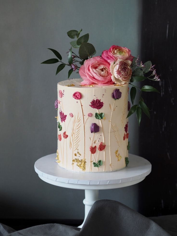 a white cake with pink flowers and greenery on top is sitting on a pedestal