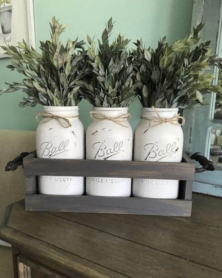 three mason jars filled with greenery sitting on top of a wooden table