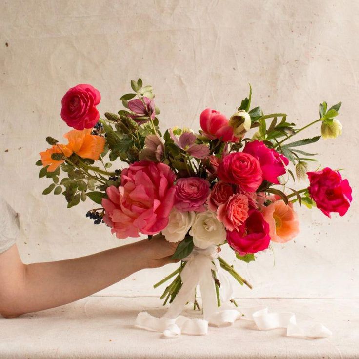 a person holding a bouquet of flowers in their hand on a white tableclothed surface