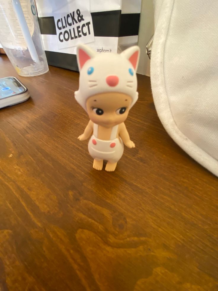 a small toy cat sitting on top of a wooden table next to a cell phone