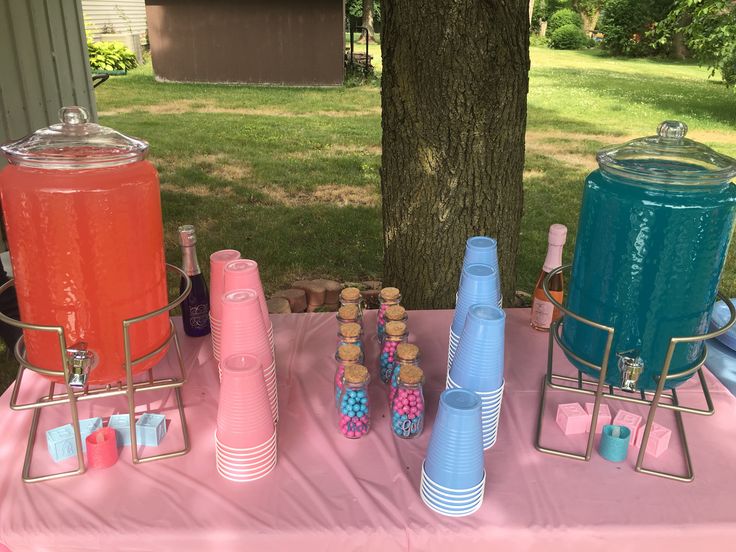 a pink table topped with lots of drinks next to a tree and grass covered field