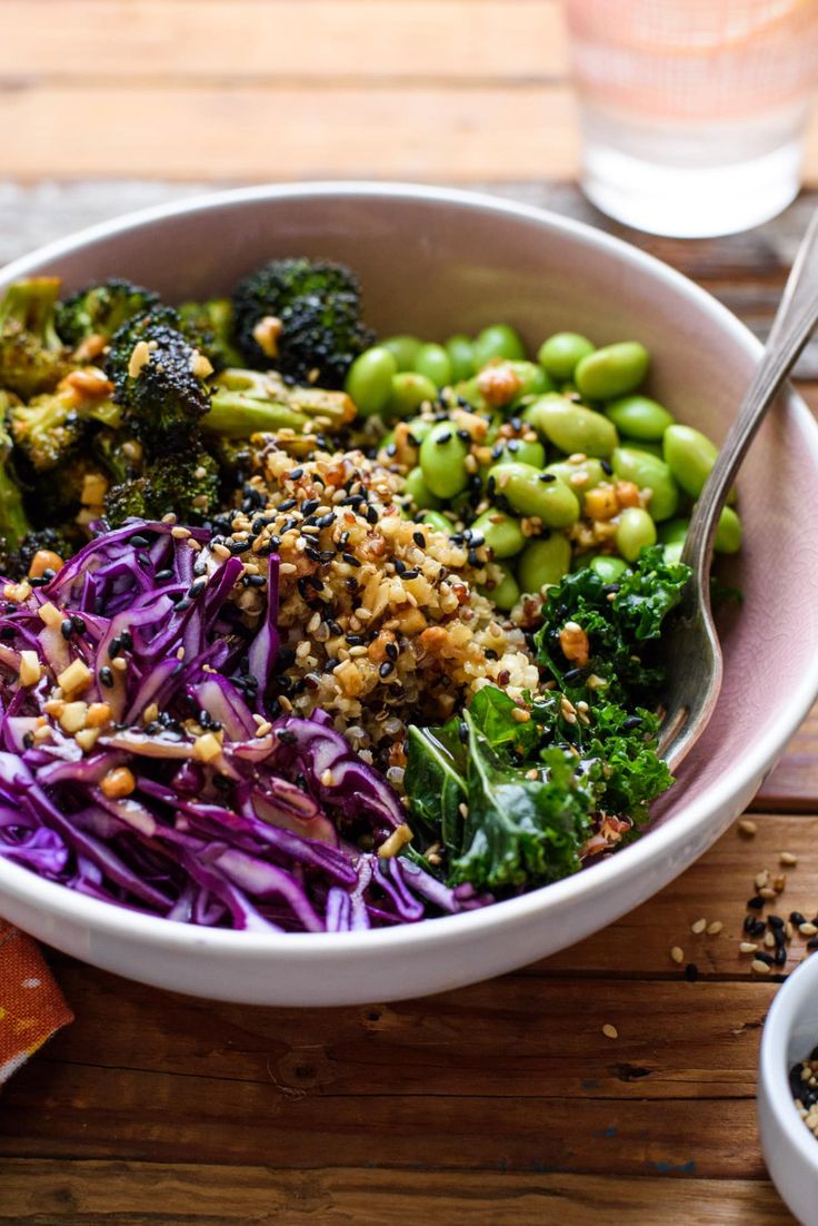 a bowl filled with broccoli, purple cabbage and sprouts next to a glass of water