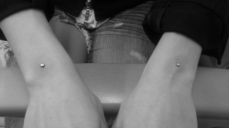 two people are sitting on a bench with their legs crossed and one is wearing small diamond studs