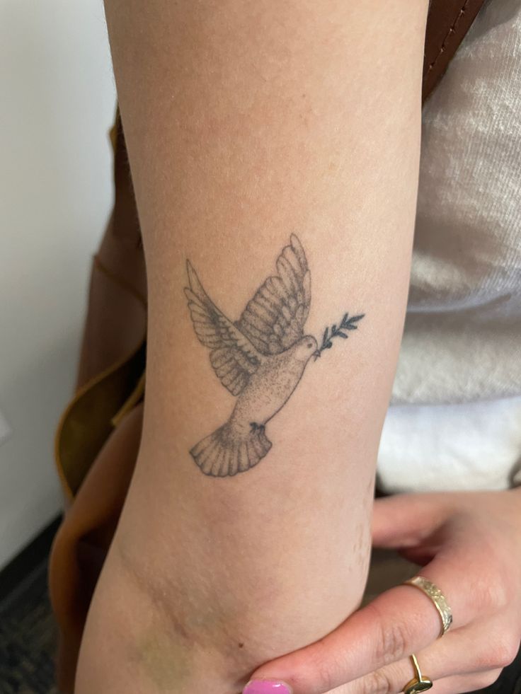 a woman with a tattoo on her arm holding a small white bird and an arrow