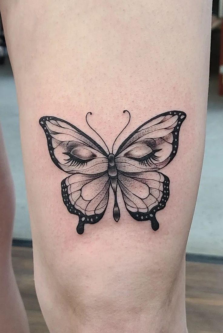 a black and white tattoo of a butterfly on the right side of the leg,