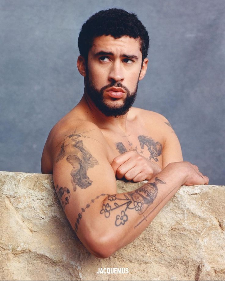 a man with tattoos on his arms leaning against a rock