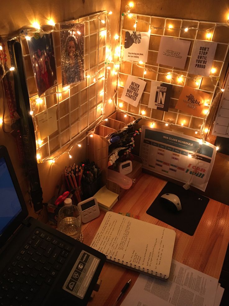 a laptop computer sitting on top of a wooden desk next to a wall covered in lights