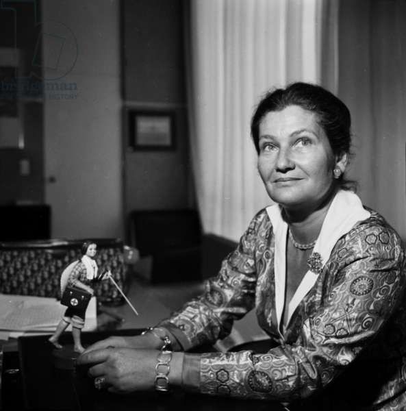 black and white photograph of woman sitting at desk with toy figurine in background