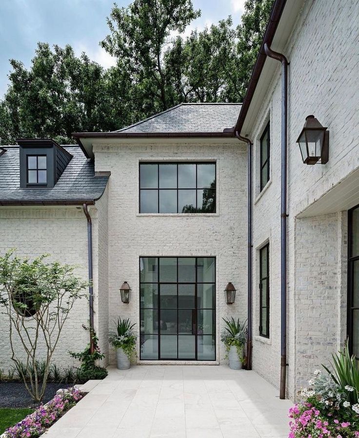 a white brick house with lots of windows and flowers in the front yard, on a sunny day