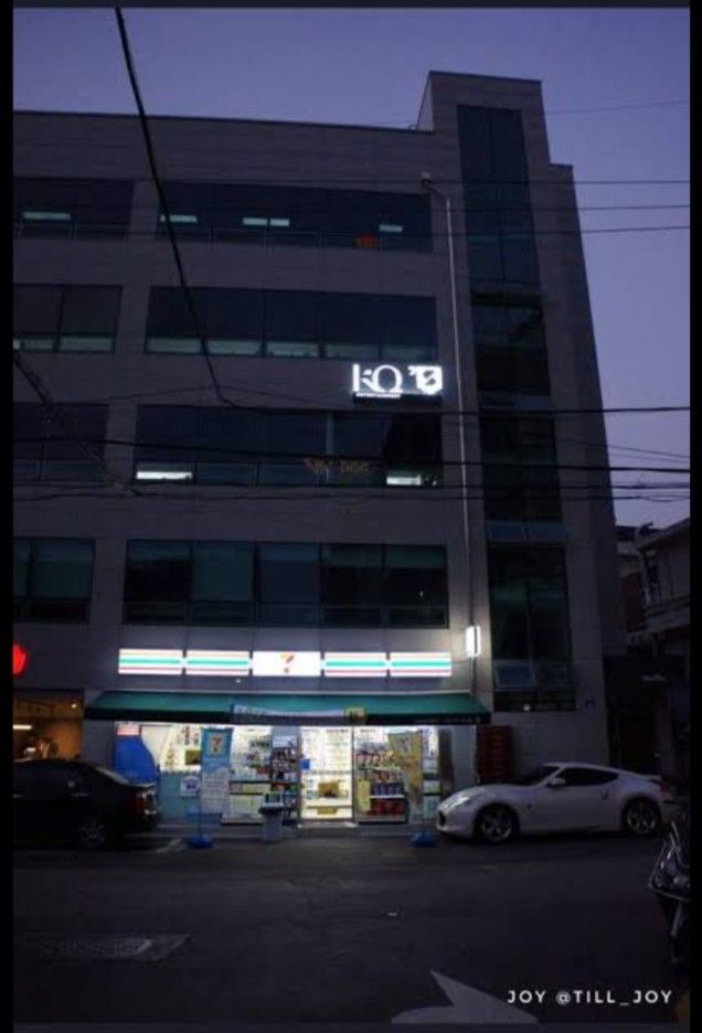 the building is lit up at night with cars parked in front and on the street