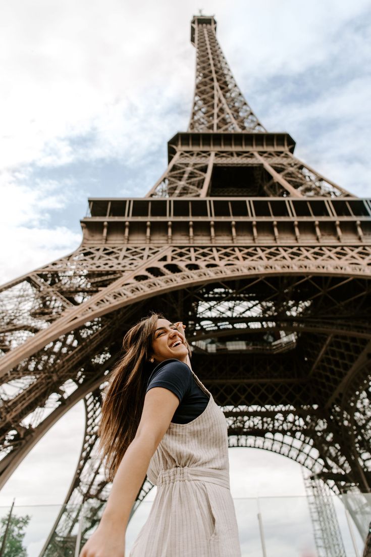 a woman standing in front of the eiffel tower, looking up into the sky