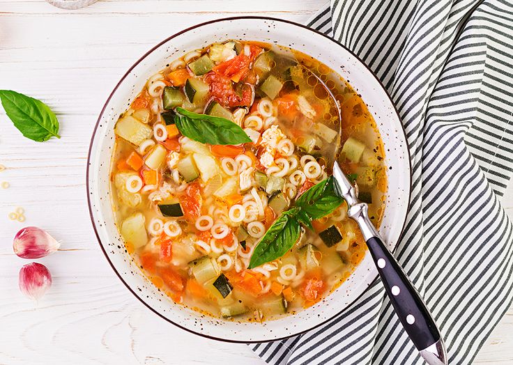 a white bowl filled with pasta and vegetables on top of a striped napkin next to a spoon